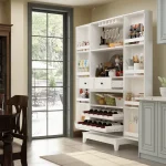 A tall, white Fufu&Gaga kitchen pantry cabinet stands against a light beige wall in a kitchen. The cabinet features two vertically paneled doors with slim black handles.