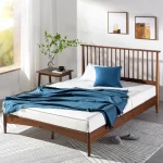 A wooden mid-century platform bed with bedding and a throw.